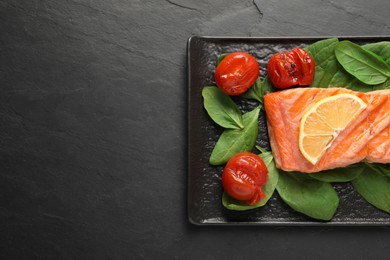 Photo of Tasty grilled salmon with tomatoes, spinach and lemon on black table, top view. Space for text