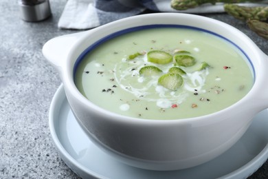 Photo of Bowl of delicious asparagus soup on grey table, closeup