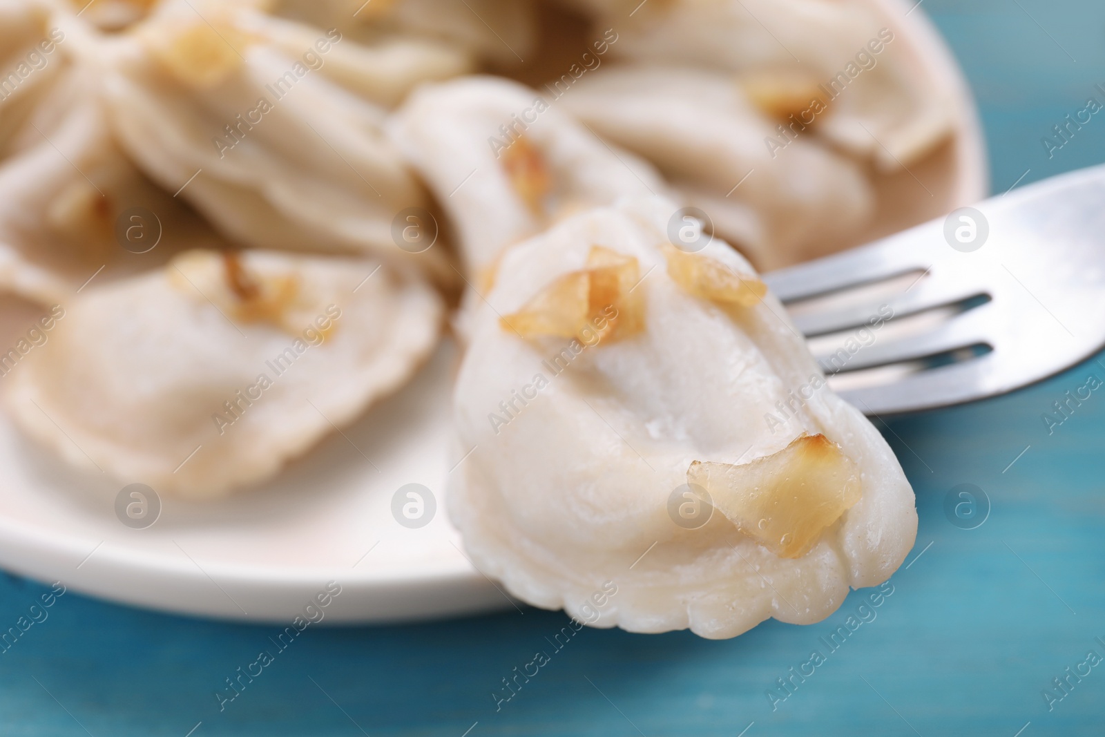 Photo of Fork with delicious dumpling (varenyky) at light blue table, closeup