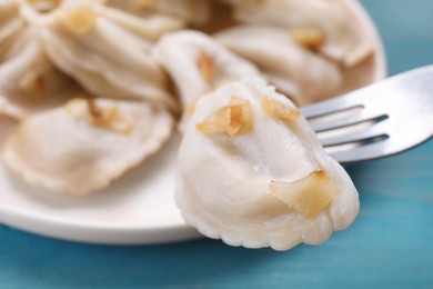 Fork with delicious dumpling (varenyky) at light blue table, closeup