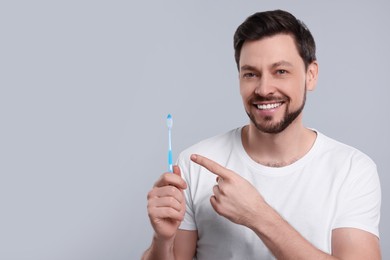 Photo of Happy man holding toothbrush on light grey background. Space for text