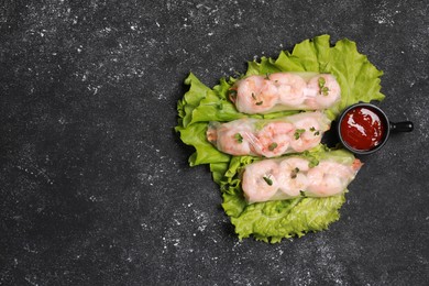 Photo of Tasty spring rolls served with lettuce, sauce and microgreens on grey textured table, flat lay. Space for text