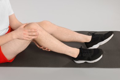 Photo of Man suffering from leg pain on mat against grey background, closeup