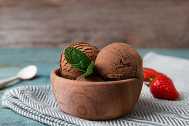 Photo of Wooden bowl of chocolate ice cream with mint and strawberry on table