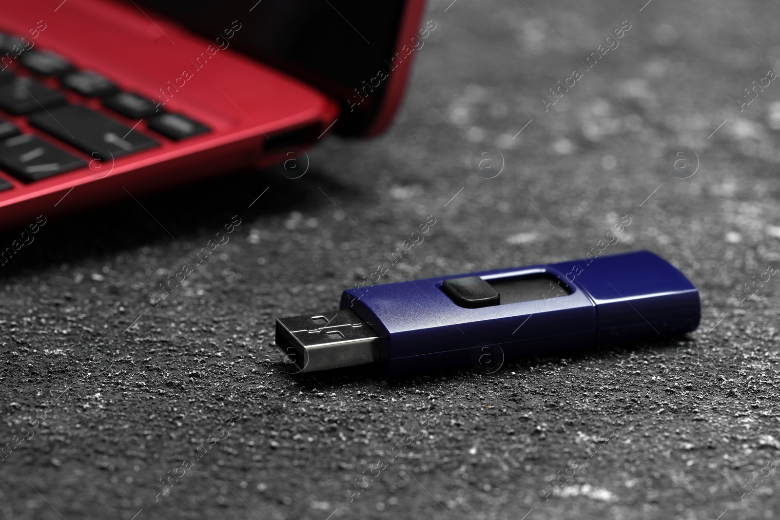 Photo of Usb flash drive near laptop on grey textured table, closeup