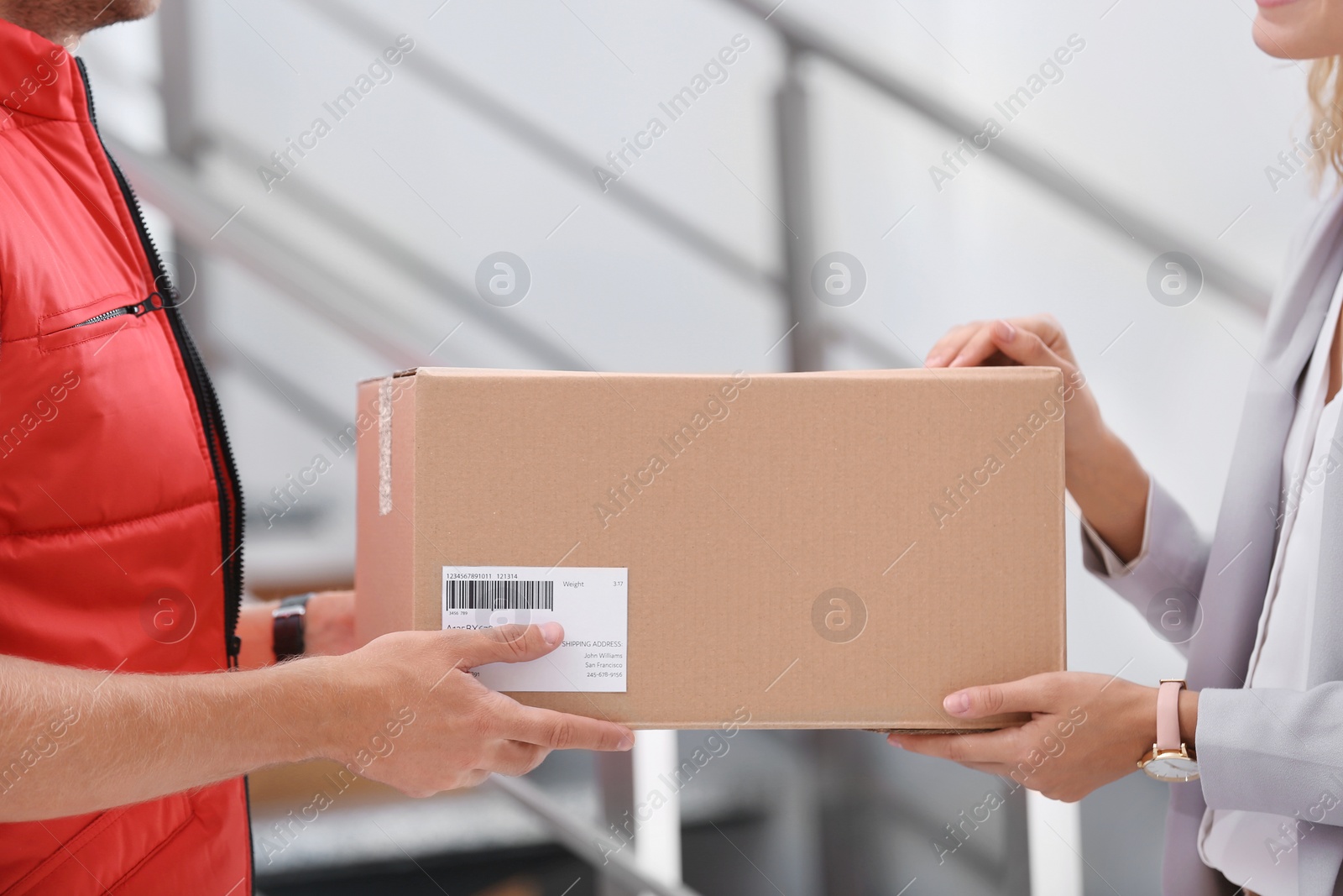 Photo of Young woman receiving parcel from courier indoors