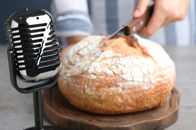 Photo of Woman making ASMR sounds with microphone and bread at grey table, closeup