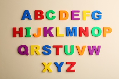 Colorful magnetic letters on beige background, flat lay. Alphabetical order