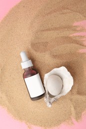 Bottle of serum, stone and seashell on sand against pink background, flat lay