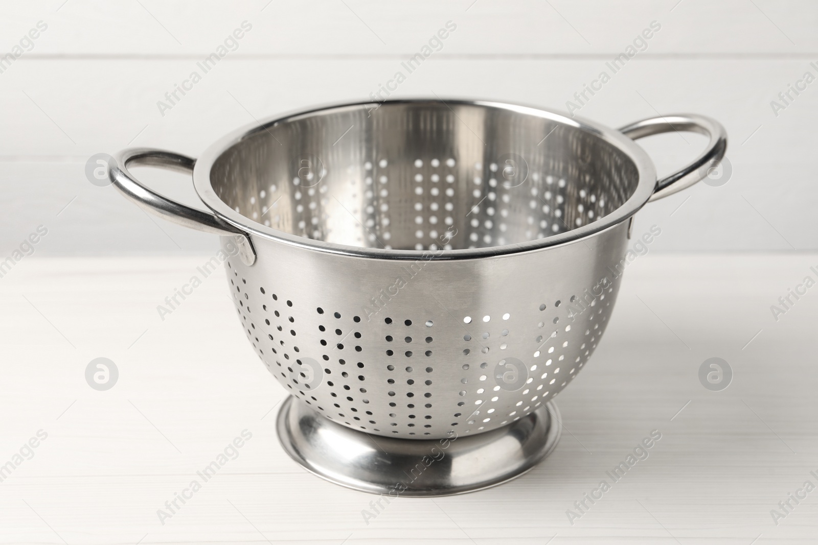 Photo of One metal colander on white wooden table