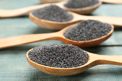 Poppy seeds in spoons on blue wooden table, closeup