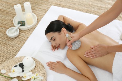 Photo of Young woman receiving herbal bag massage in spa salon