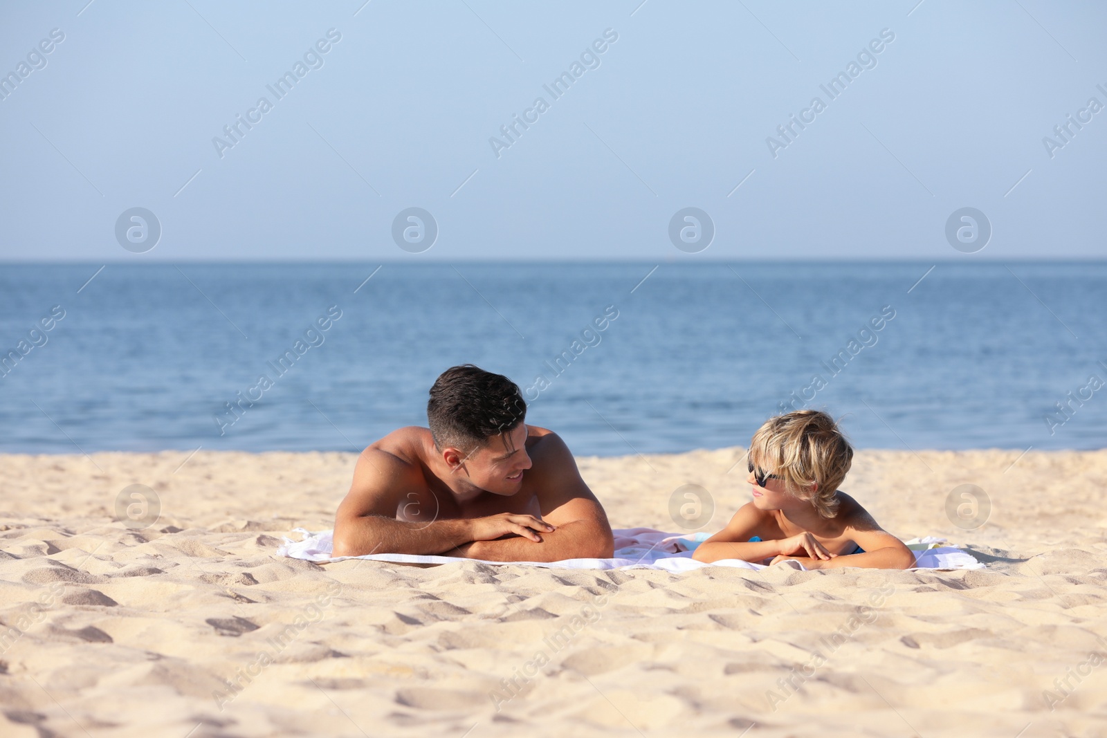 Photo of Father and son lying on sandy beach near sea. Summer holidays with family