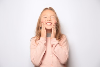 Photo of Happy little girl touching cheeks on white background