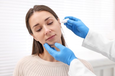 Doctor applying medical drops into woman's ear indoors