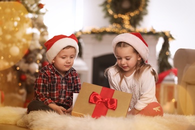 Cute children opening gift box in room decorated for Christmas