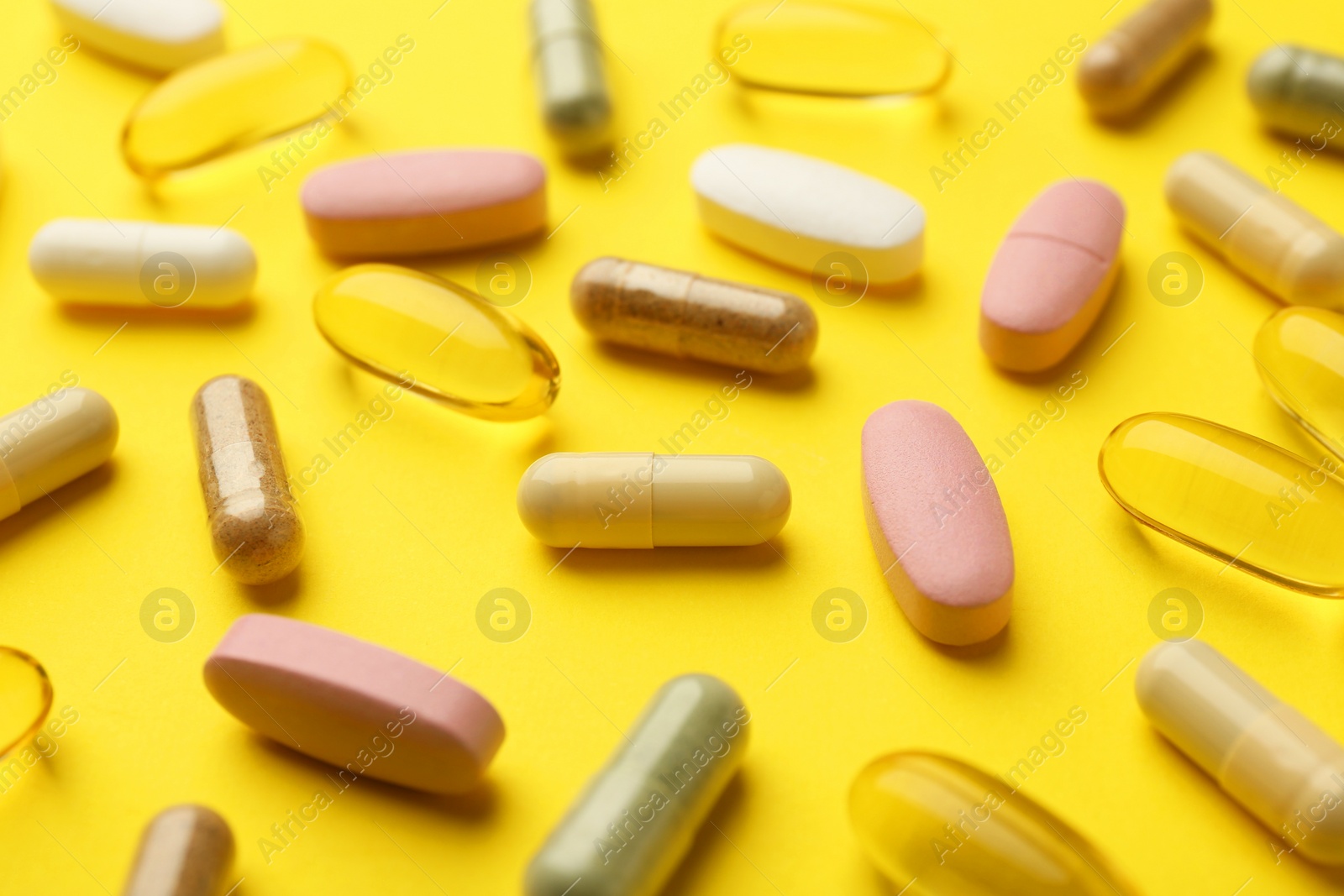 Photo of Different vitamin pills on yellow background, closeup