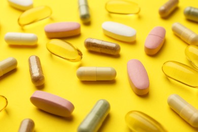 Different vitamin pills on yellow background, closeup