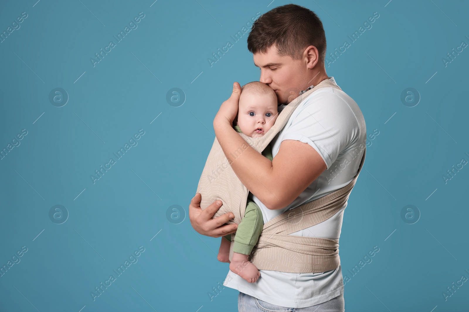 Photo of Father holding his child in sling (baby carrier) on light blue background. Space for text