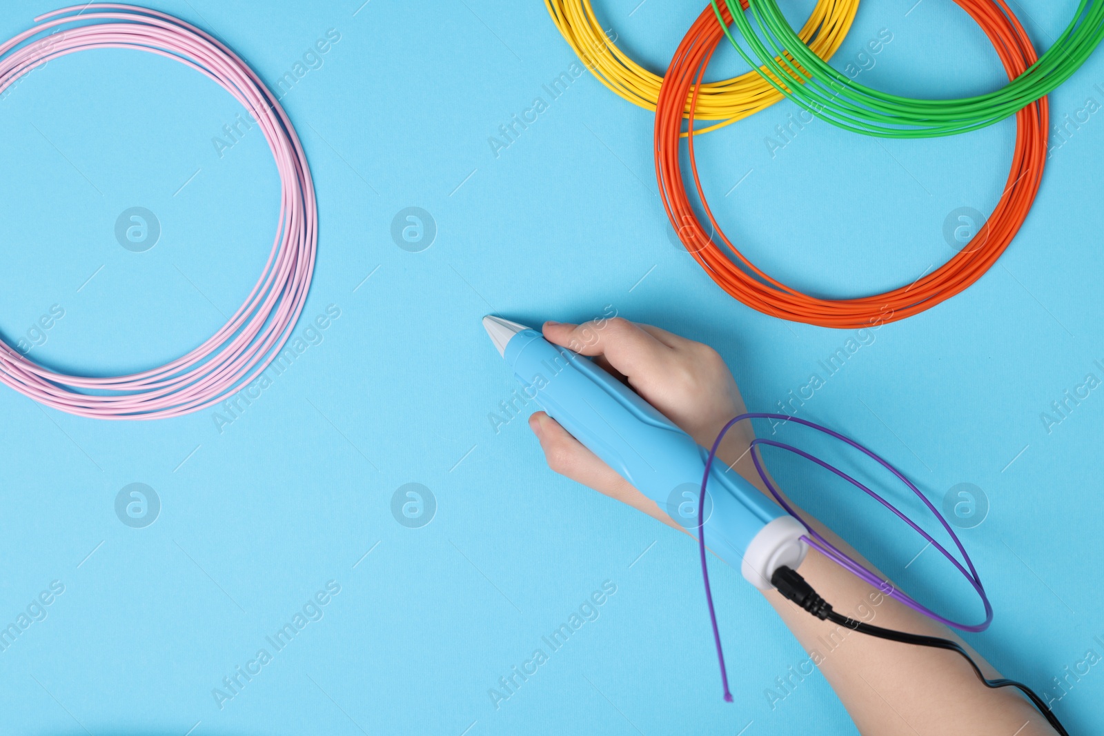 Photo of Boy drawing with stylish 3D pen on light blue background, top view