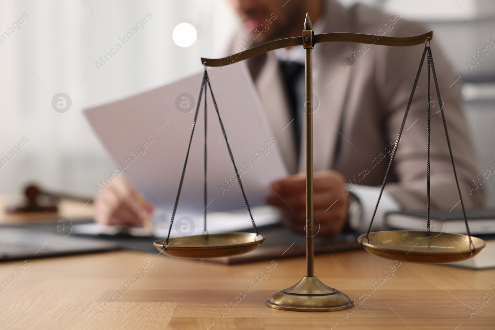 Photo of Lawyer working with document at table in office, focus on scales of justice