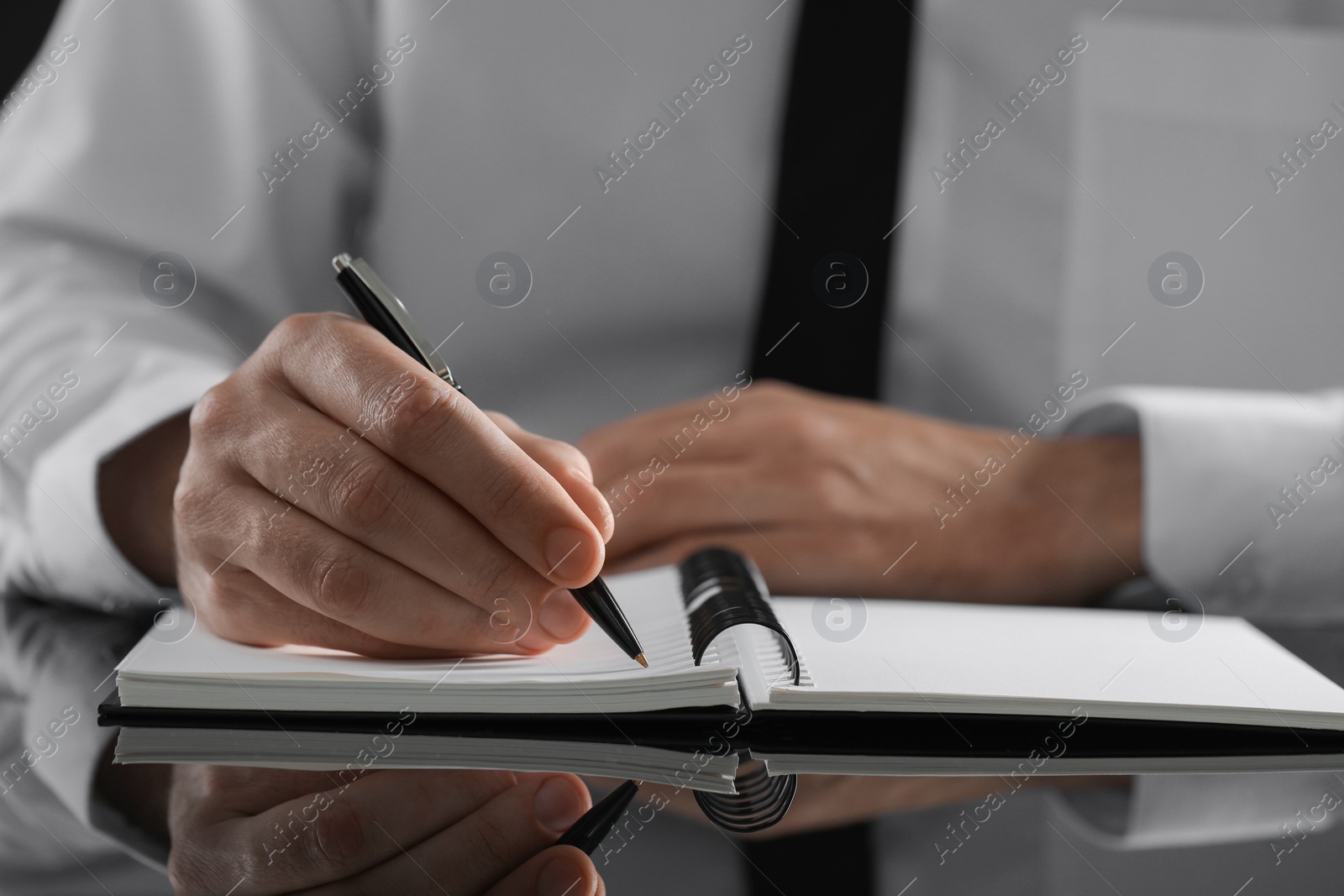 Photo of Man writing in notebook at black table, closeup. Space for text