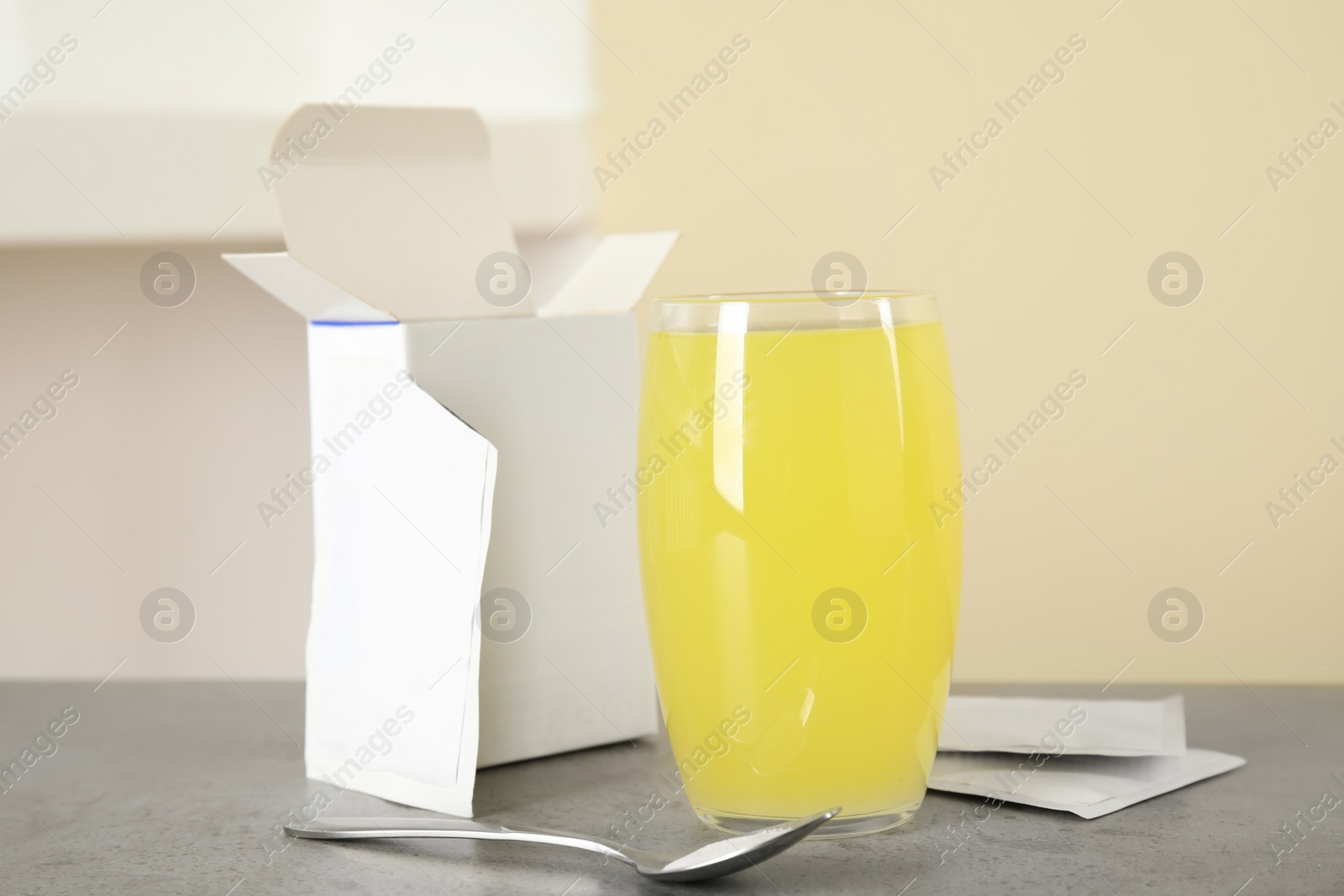 Photo of Glass with dissolved drug, medicine sachets and spoon on grey table