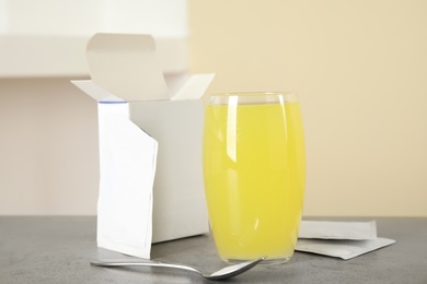 Glass with dissolved drug, medicine sachets and spoon on grey table