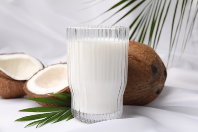 Photo of Glassdelicious coconut milk, palm leaves and coconuts on white fabric