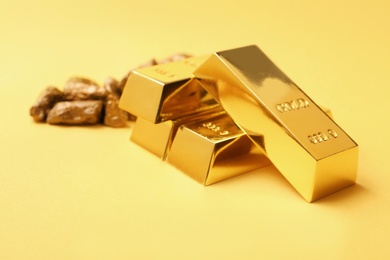 Gold nuggets and ingots on color background