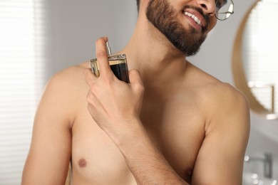 Photo of Young man spraying luxury perfume indoors, closeup