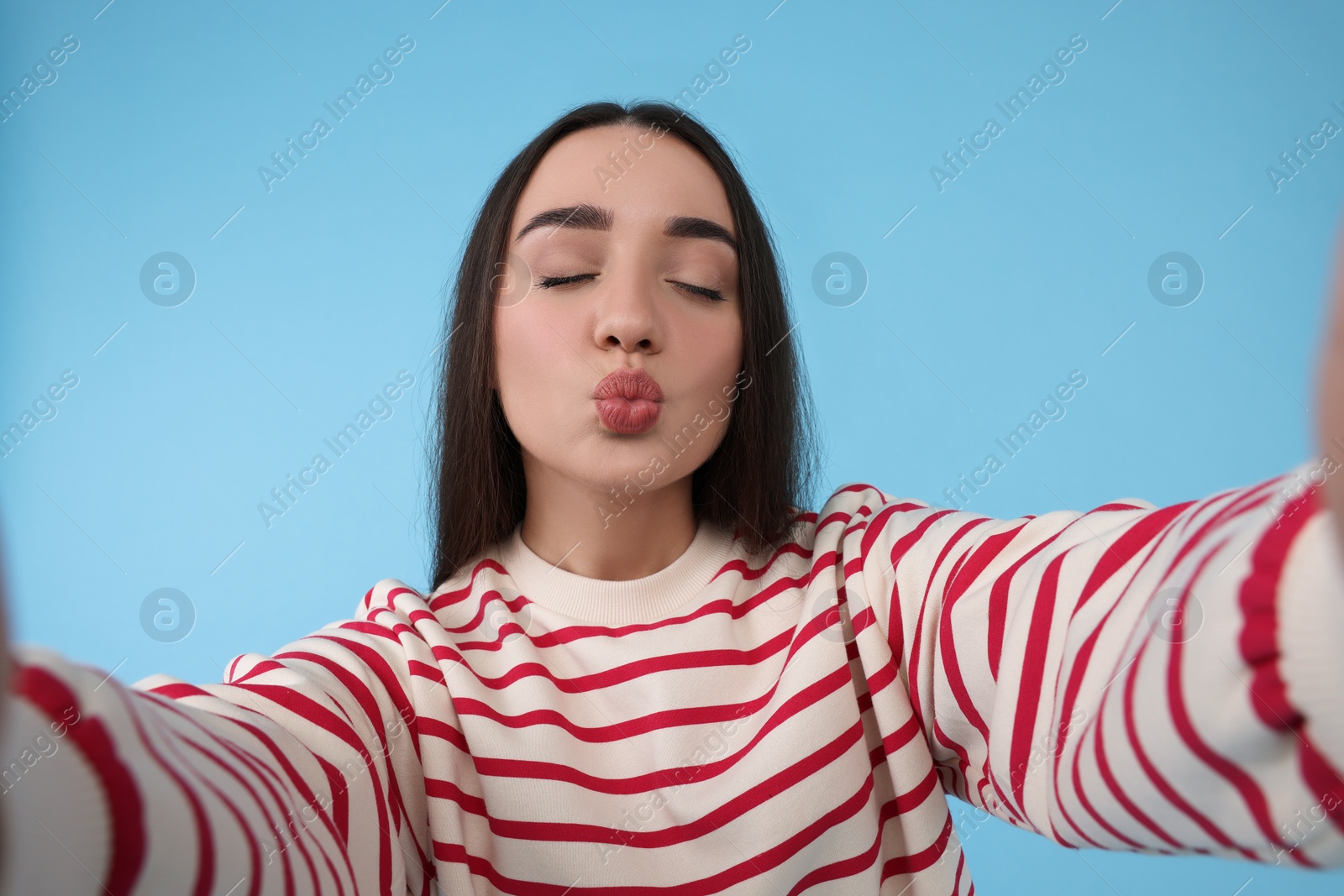 Photo of Young woman taking selfie and blowing kiss on light blue background