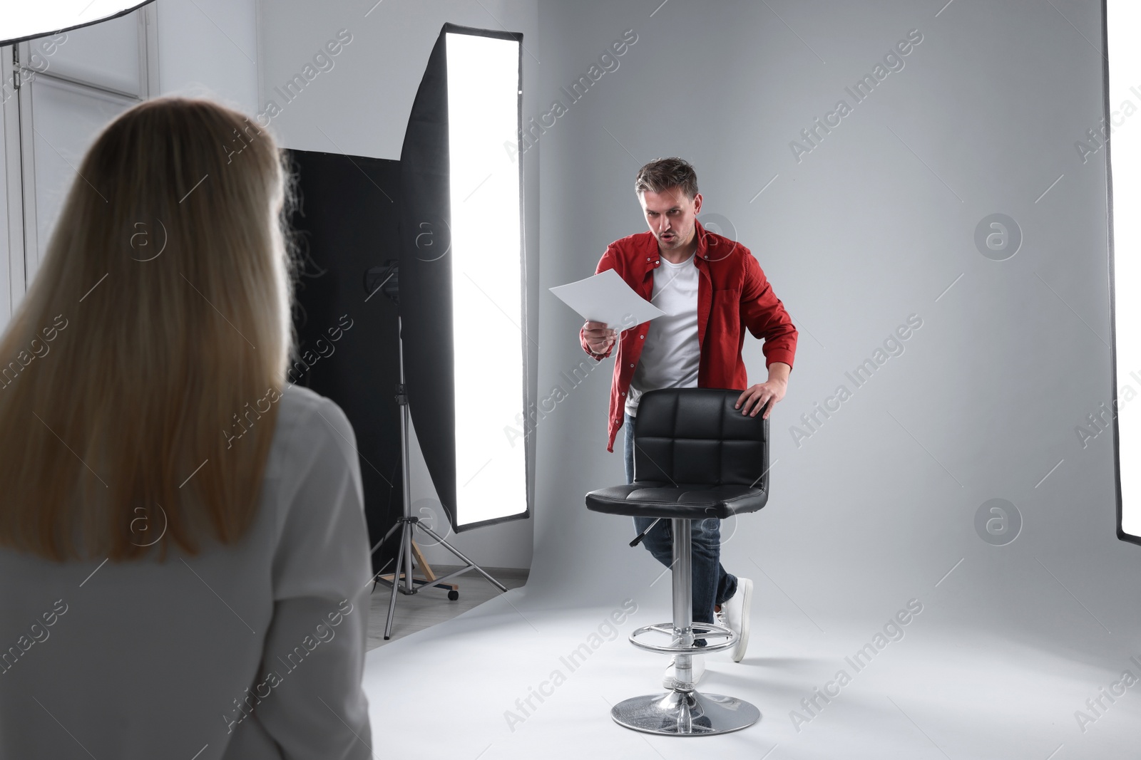 Photo of Emotional man with script performing in front of casting director against light grey background in studio