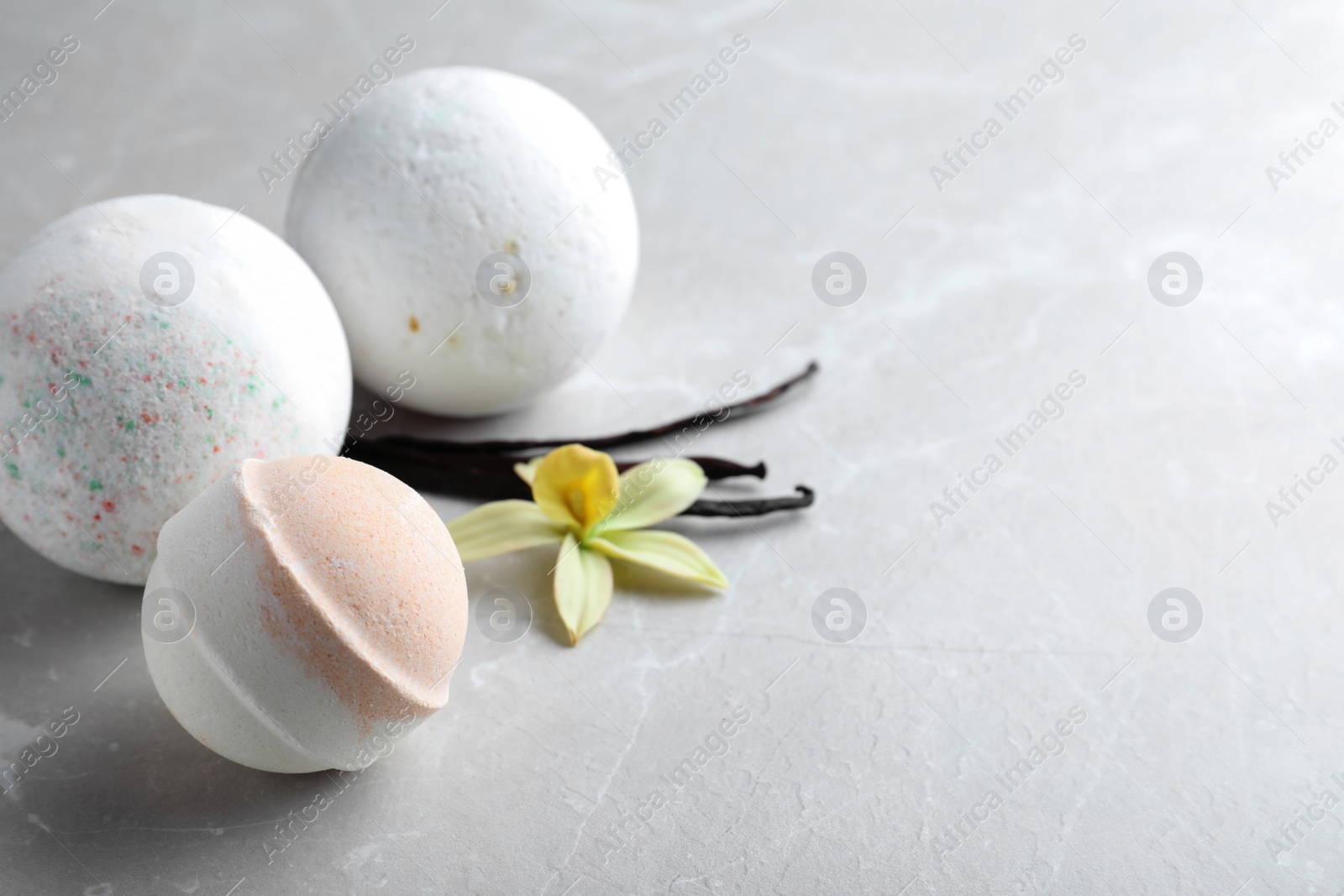 Photo of Fragrant bath bombs, vanilla sticks and flower on light grey table. Space for text