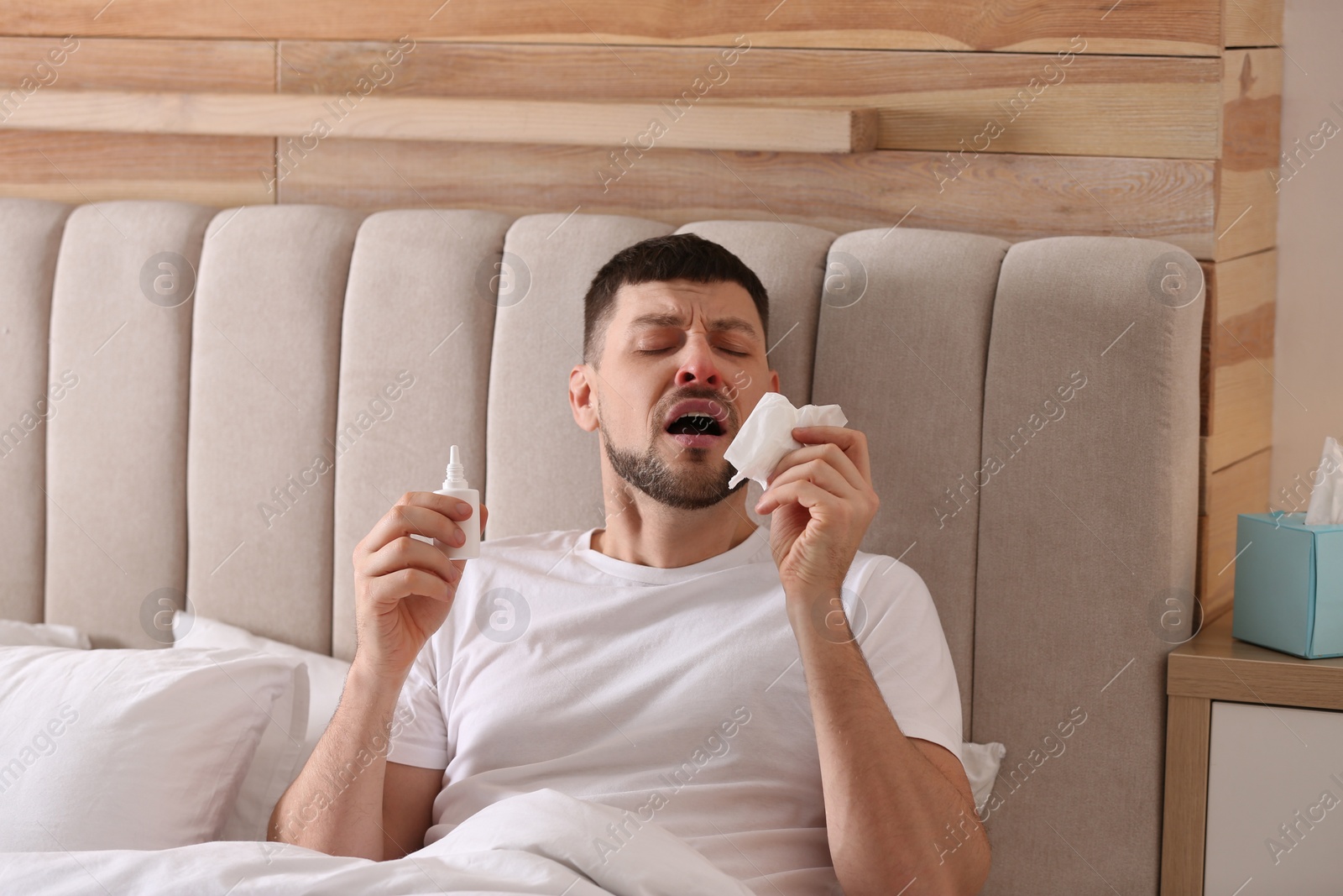 Photo of Ill man with nasal spray and paper tissue in bed at home