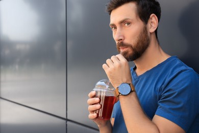 Photo of Handsome man drinking delicious juice near grey wall outdoors. Space for text