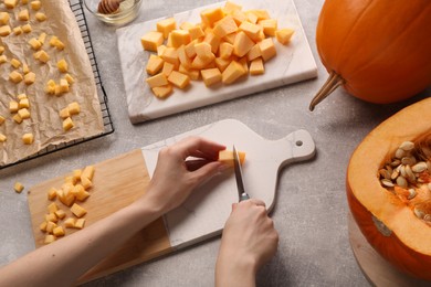 Photo of Woman cutting fresh pumpkin at light grey table, closeup