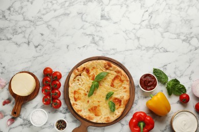 Delicious khachapuri with cheese surrounded by different products on white marble table, flat lay. Space for text