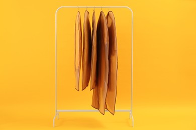 Photo of Garment bags with clothes on rack against yellow background