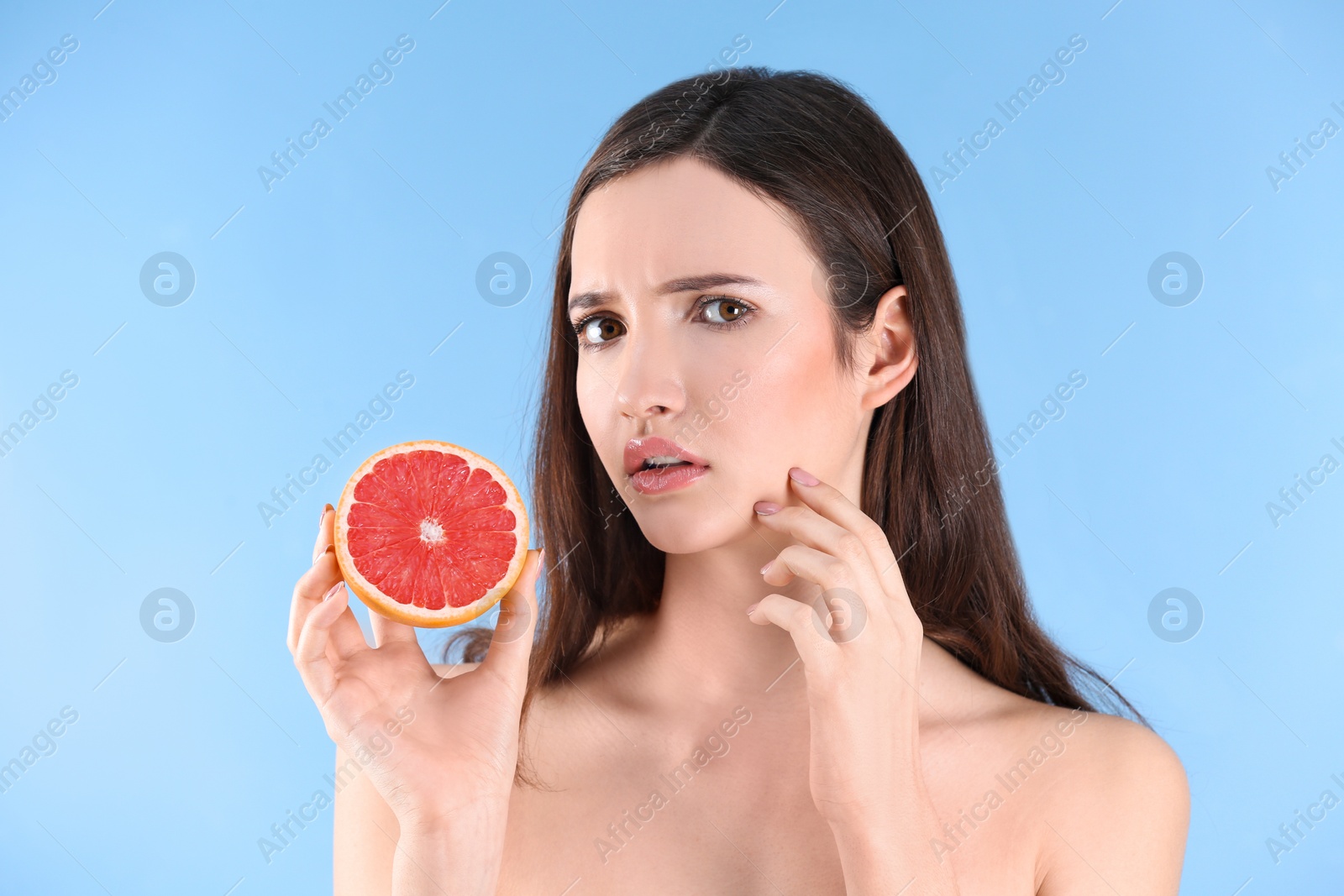 Photo of Teenage girl with acne problem holding grapefruit against color background