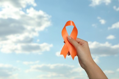 Photo of Woman holding orange ribbon against blue sky, closeup with space for text. Multiple sclerosis awareness
