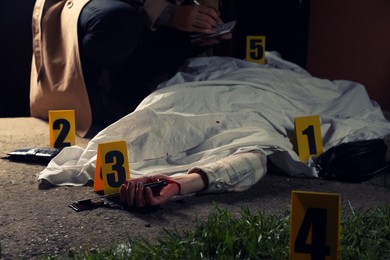 Photo of Investigator examining crime scene with dead body outdoors, closeup