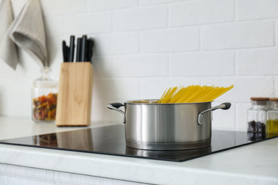 Photo of Saucepan with uncooked pasta on stove in kitchen