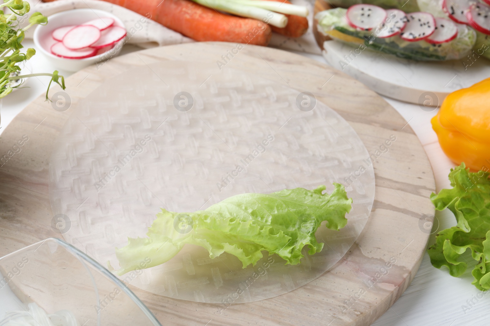 Photo of Rice paper and other ingredients for spring rolls on white wooden table