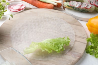 Rice paper and other ingredients for spring rolls on white wooden table