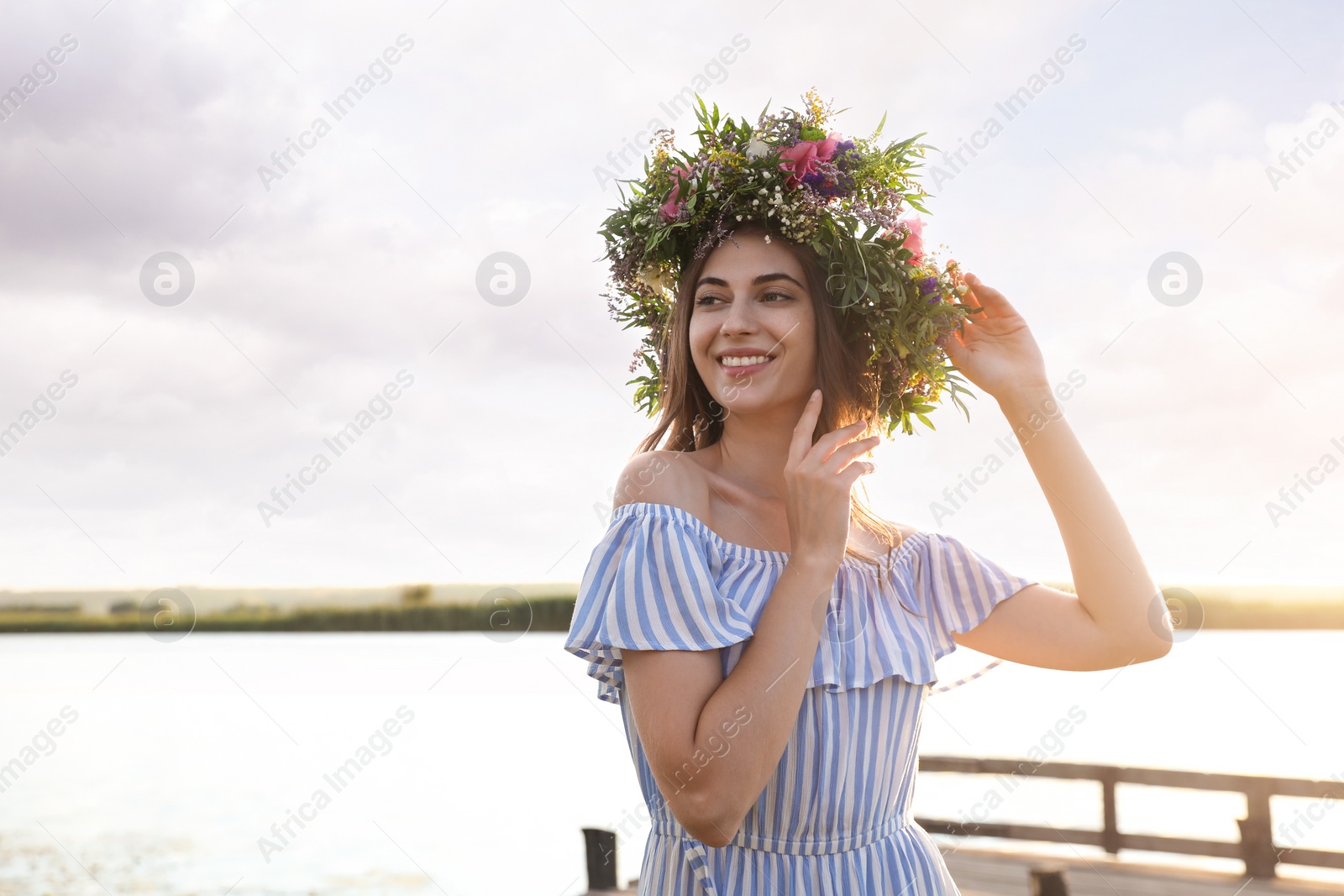 Photo of Young woman wearing wreath made of beautiful flowers near river on sunny day