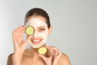 Photo of Beautiful woman holding cucumber slices near her face with clay mask against grey background. Space for text
