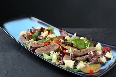 Photo of Delicious salad with beef tongue and cheese on black textured table, closeup