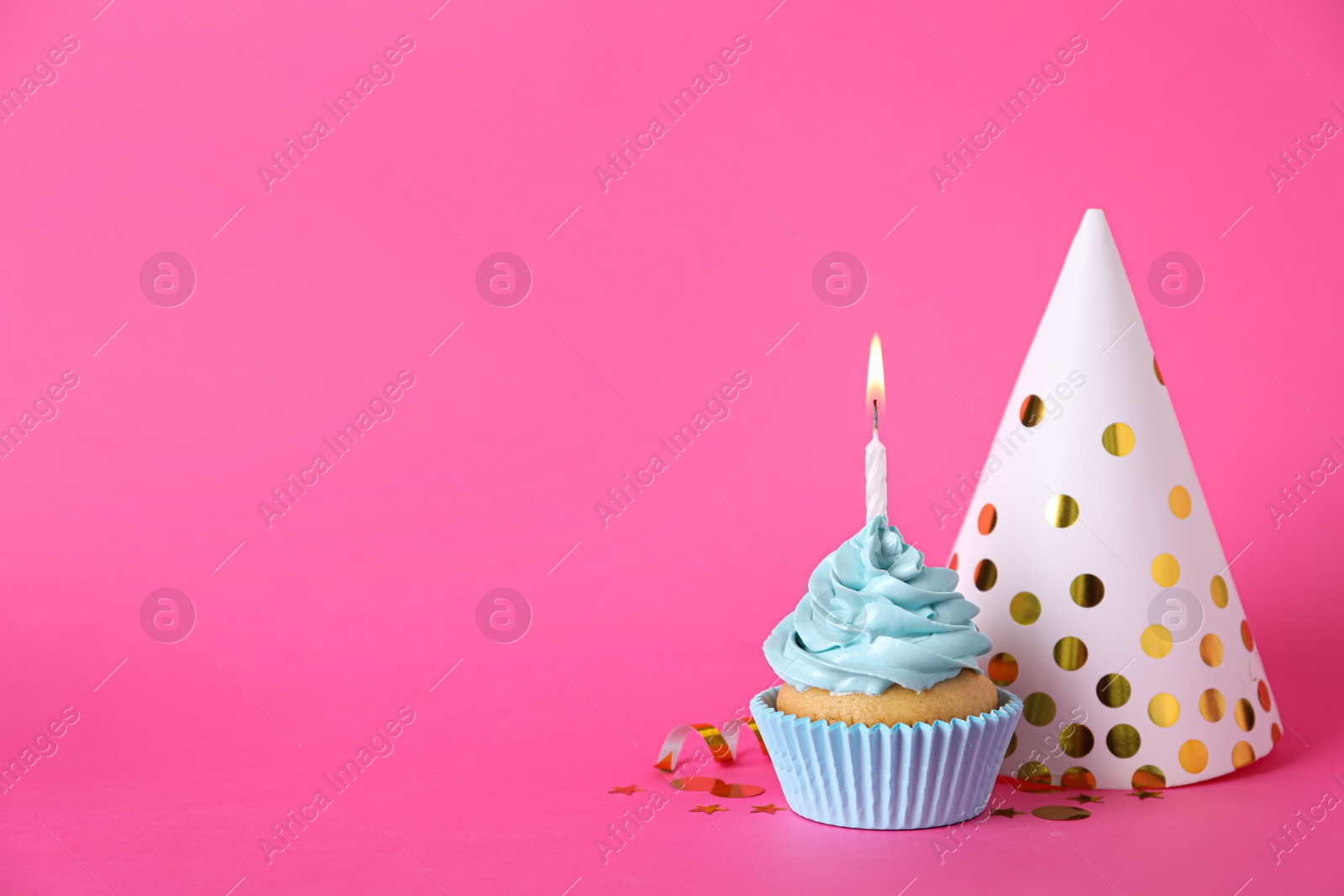 Photo of Delicious birthday cupcake with burning candle, party hat and confetti on pink background, space for text