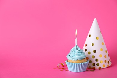 Delicious birthday cupcake with burning candle, party hat and confetti on pink background, space for text